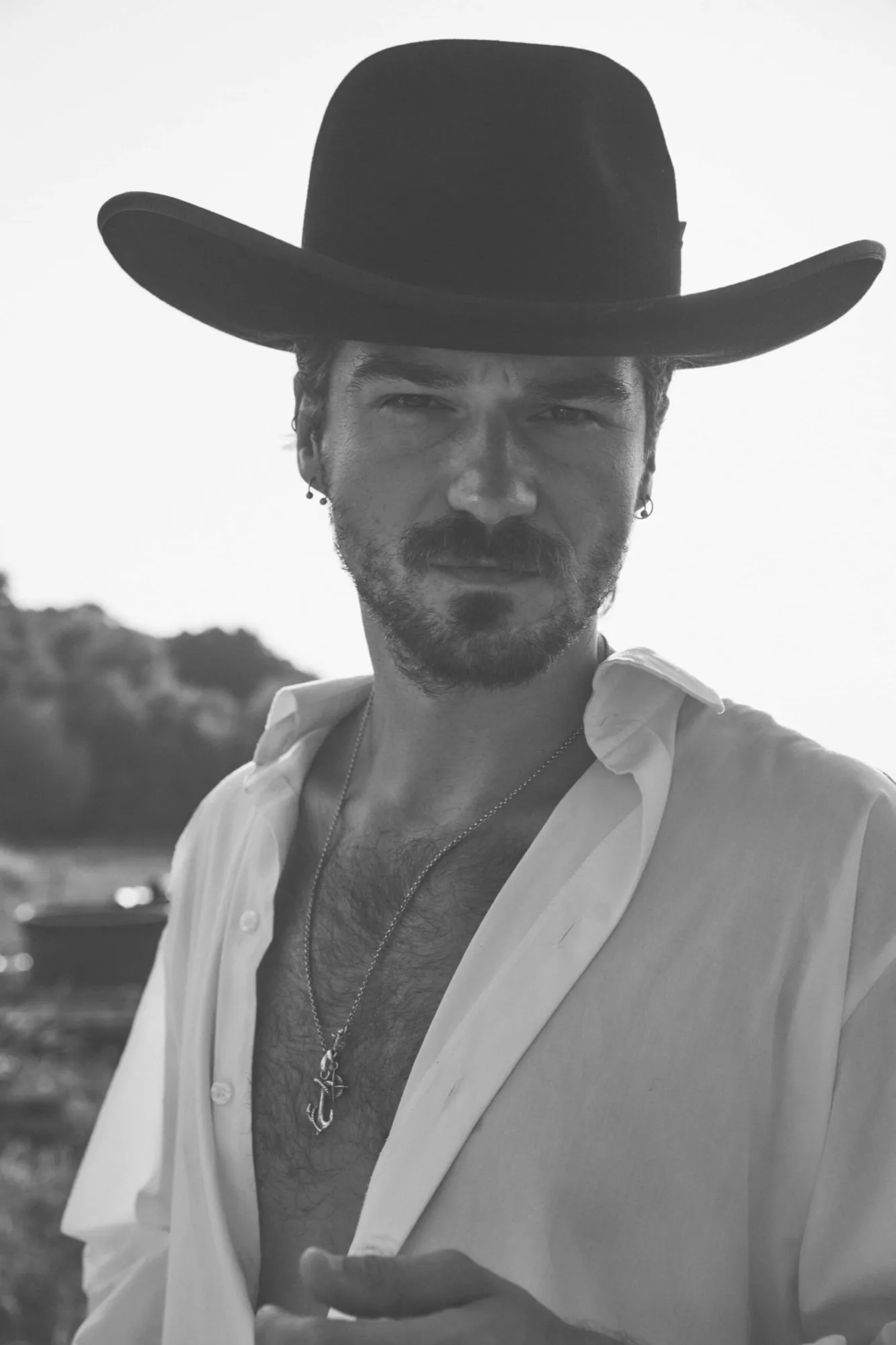 Man in a black cowboy hat and open white shirt, black and white