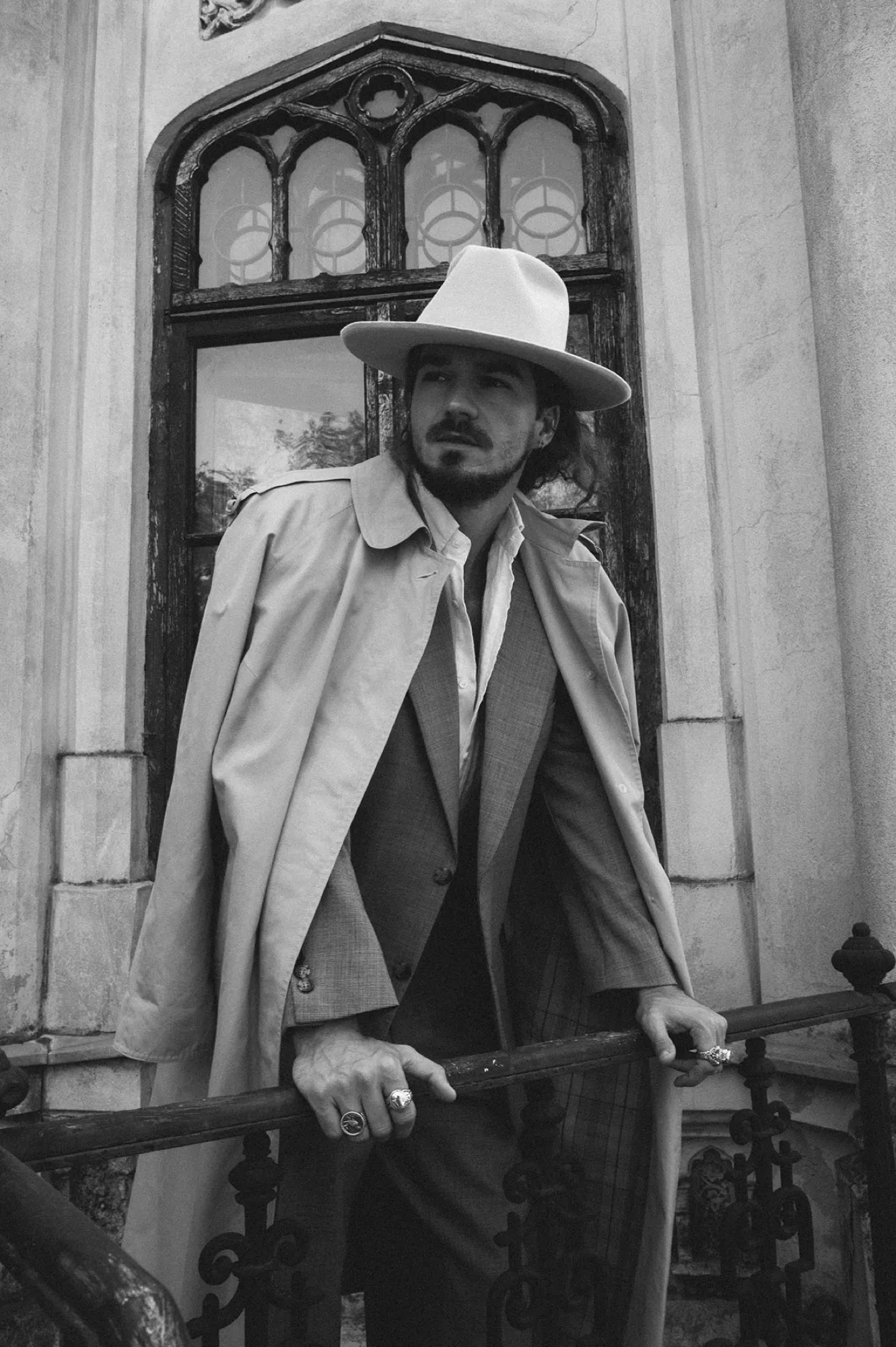 Man in a pale hat and long coat in a gothic doorway