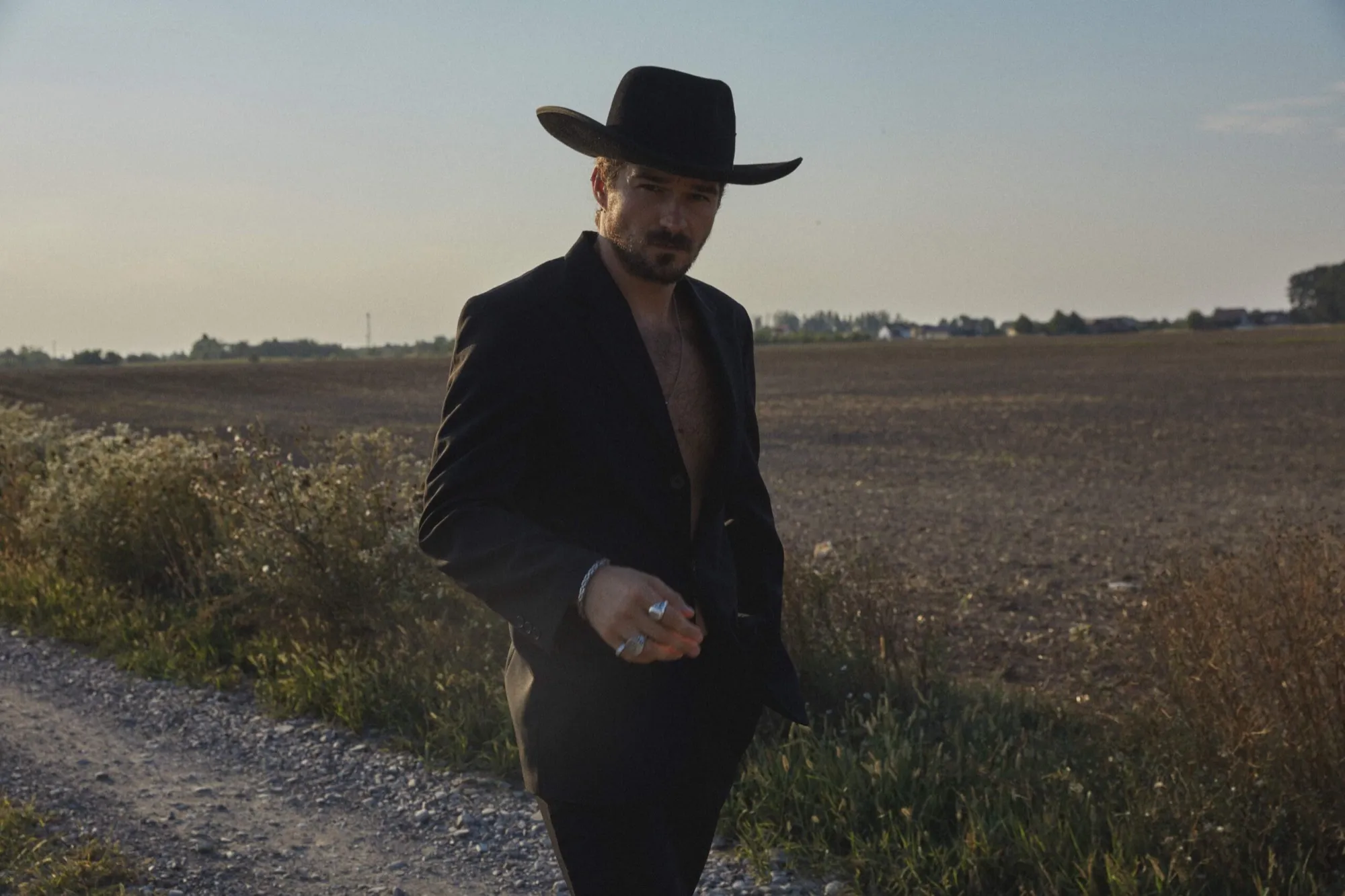 Man in a black hat standing in a field at dusk