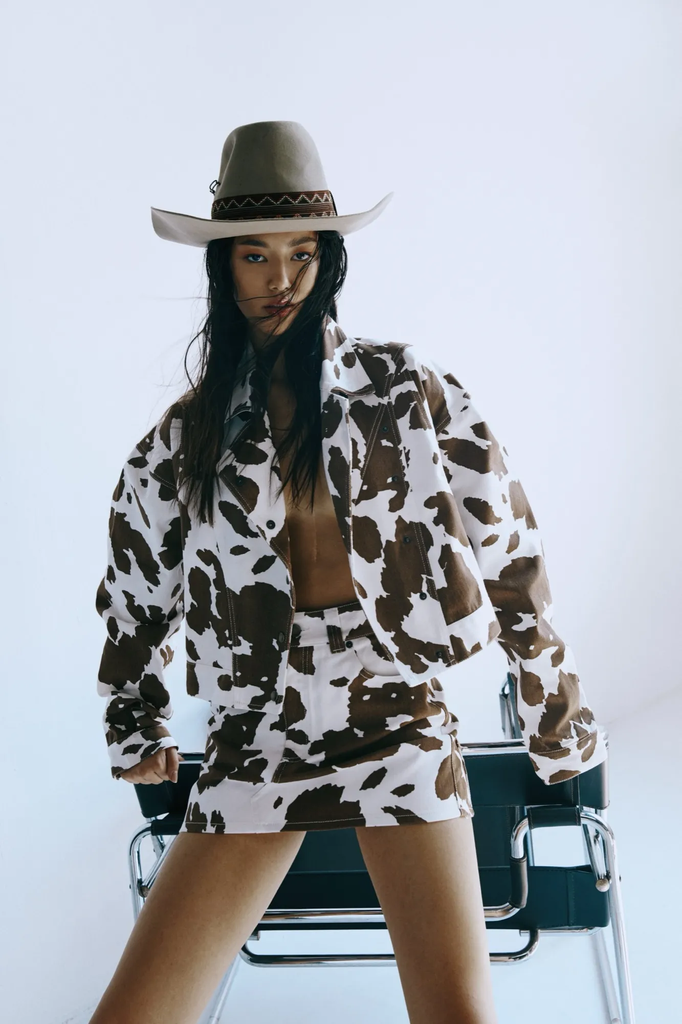 Woman in a cow-print outfit and pale hat, seated