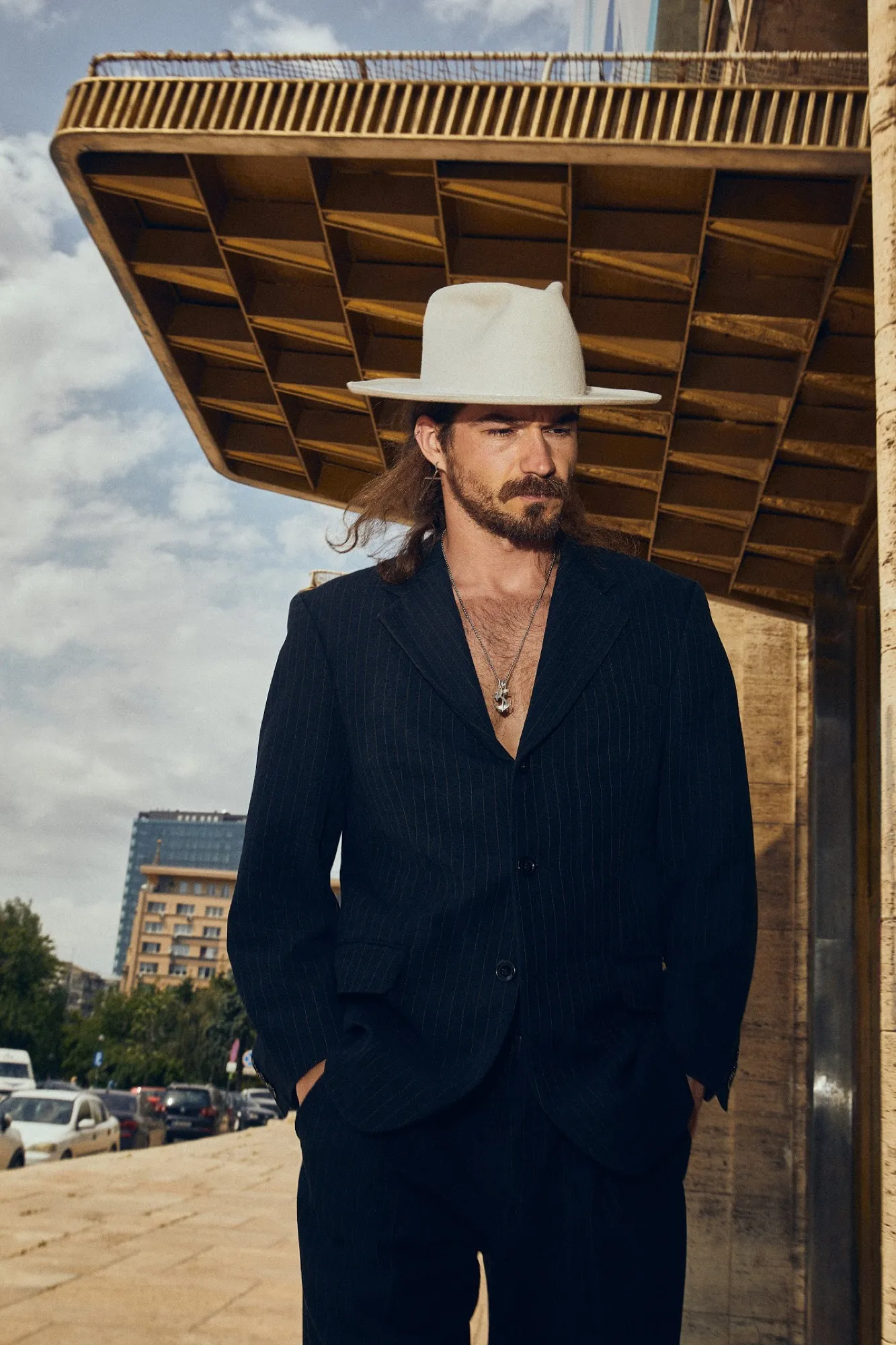 Man in a white hat and navy suit under a concrete canopy