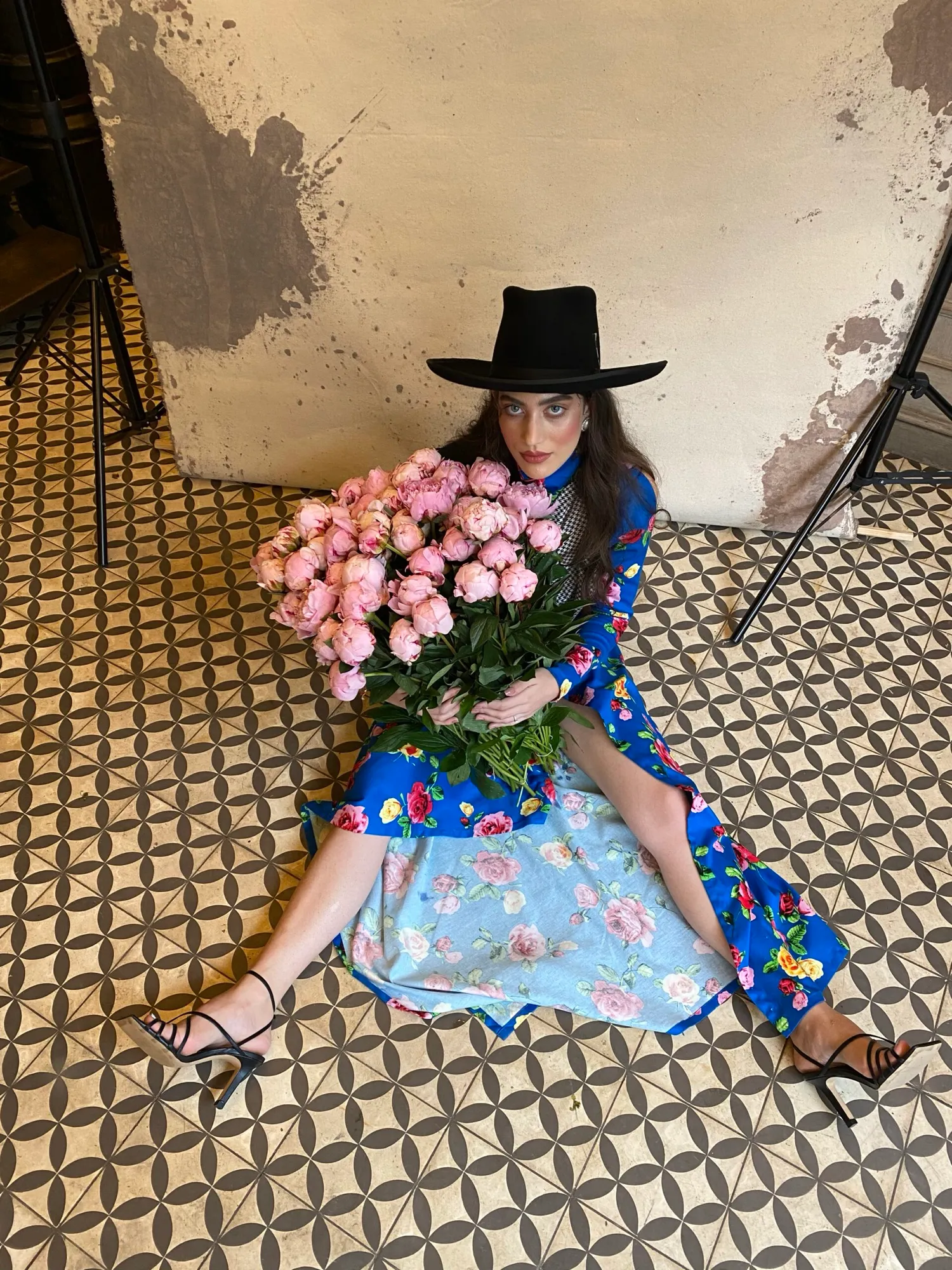 Woman seated on a tiled floor with pink roses, wearing a black hat