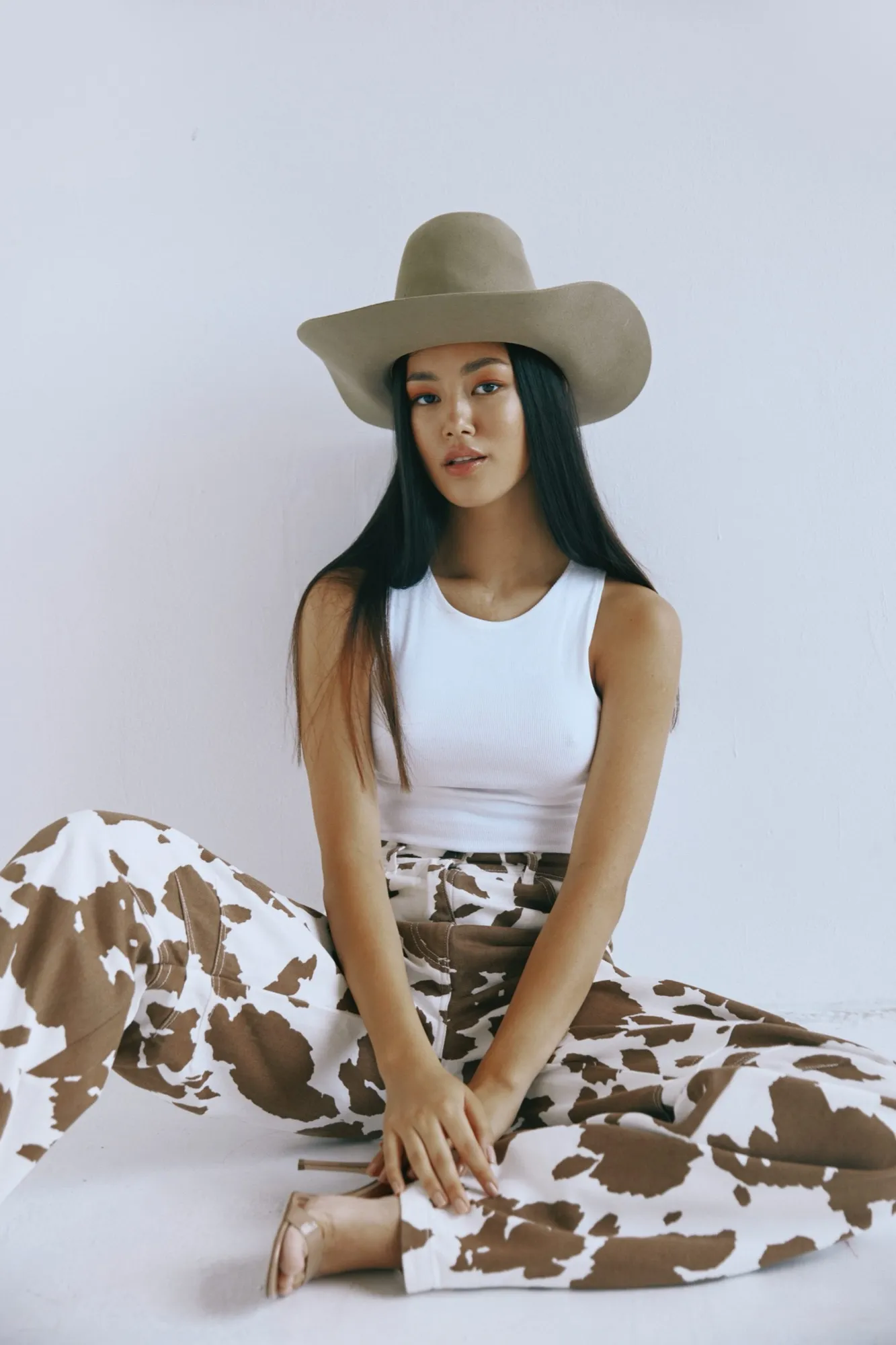 Woman in a white top and cow-print trousers wearing a pale hat